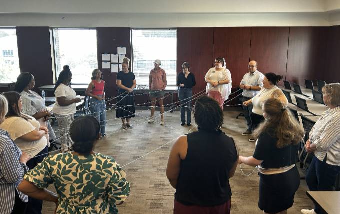 A group of people standing in a circle holding yarn pieces all connected together.