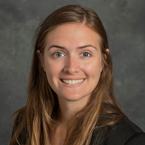 Rachel is pictured from the shoulders up wearing a black jacket. She has fair skin, long blonde hair, and is smiling at the camera. 