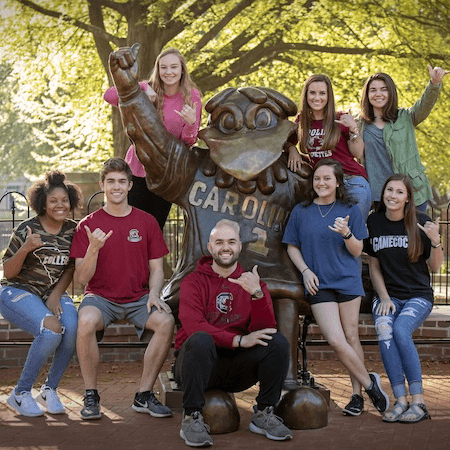 people on university campus tour standing in front cocky statue