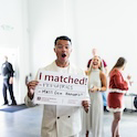 student in white suit holding sign reading "i matched"