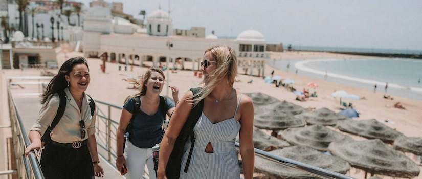 image of three students walking on a bridge in front of the ocean smiling