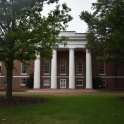 Exterior view of the front of the South Caroliniana Library. The low angle shows sunlight streaming through trees onto the red brick building and four white columns.