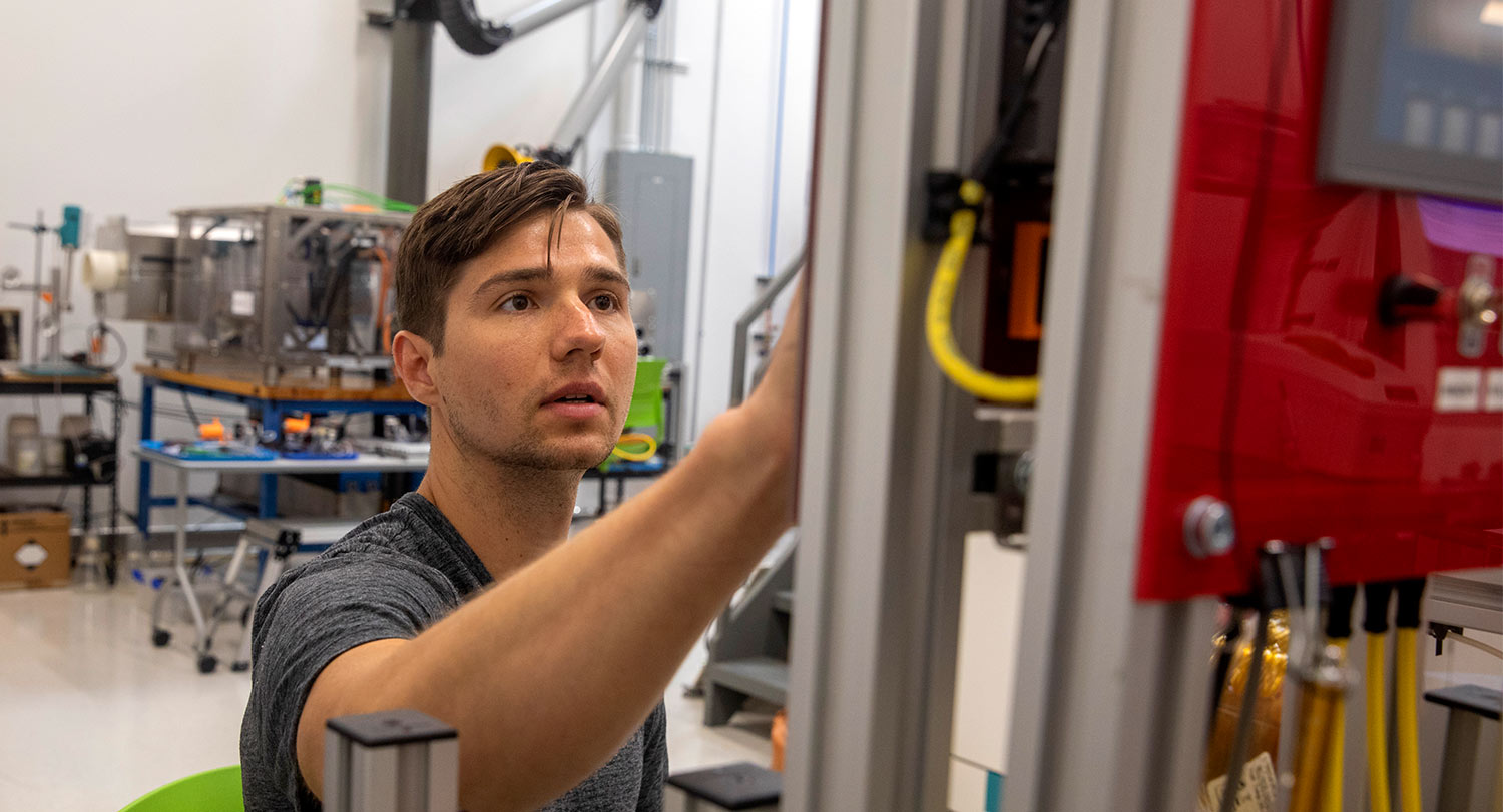 A graduate student reaches up to make adjustments on a piece of equipment. 