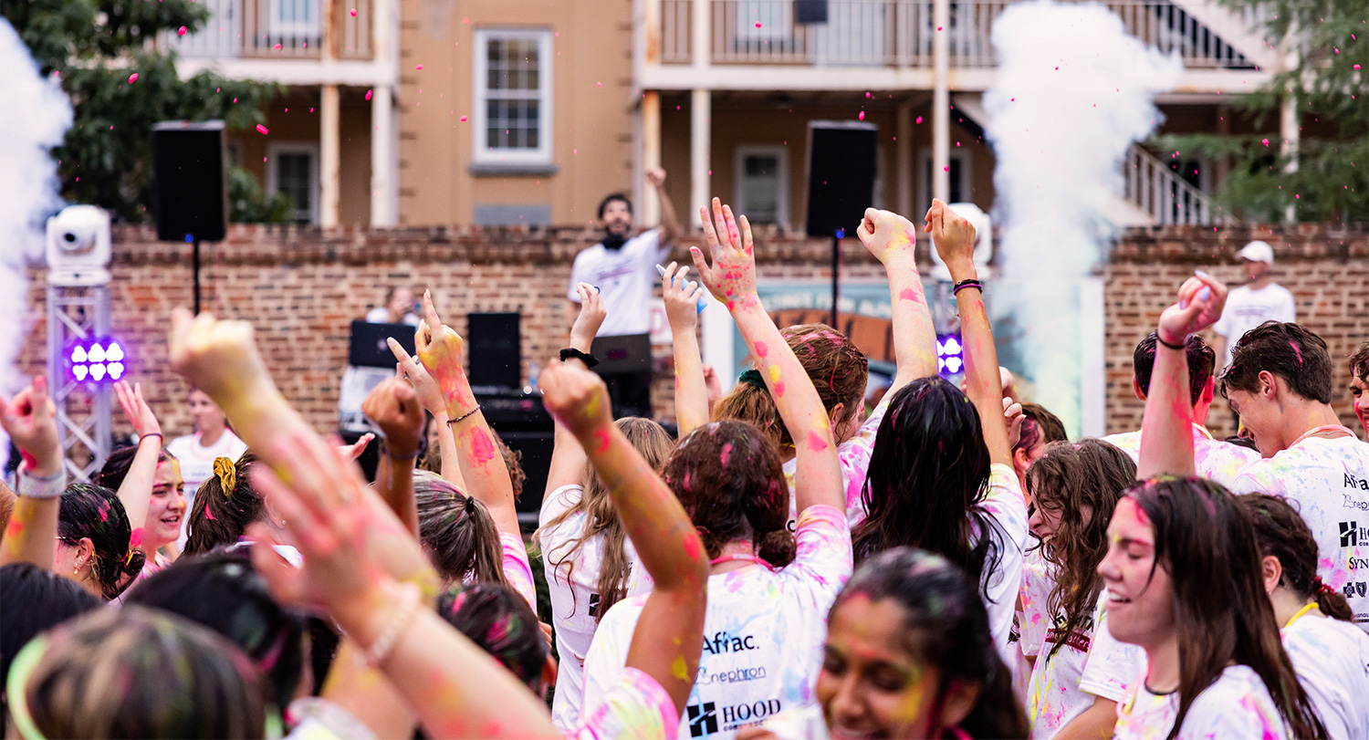 Studnets gathered together with their arms raised at an event on Greene Street.