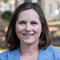 Dr. Lindsay McCary, a white woman with shoulder length brown hair, smiles at the camera for a professional headshot on the Horseshoe