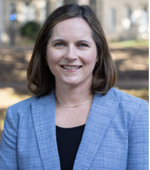 Dr. Lindsay McCary, a white woman with shoulder length brown hair, smiles at the camera for a professional headshot on the Horseshoe.
