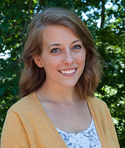 woman smiling outside with a yellow sweater on. 