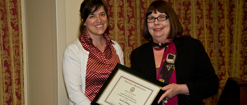 A smiling student in professional attire is being handed an award by Dr. Drue Barker.