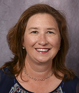 a woman in a dark shirt with brown shoulder length hair smiling