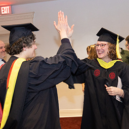 graduates in regalia slapping high five