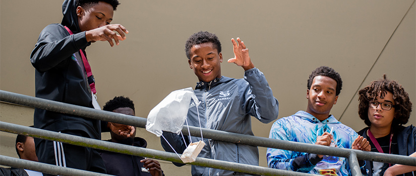 two students drop an egg parachute over railing