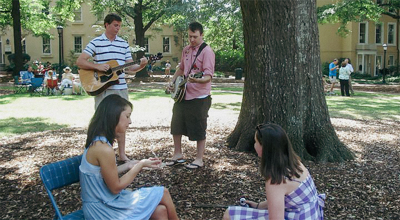 Two men playing the guitar and banjo on USC's historic Horseshoe with two women in dresses next to them.
