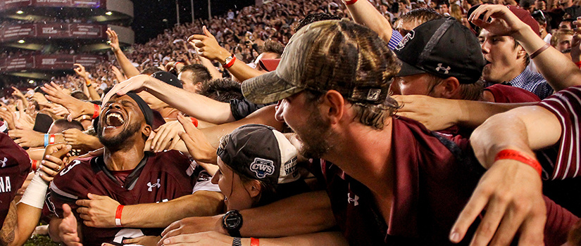 A UofSC football player on the sidelines being congratulated by fans during a game.