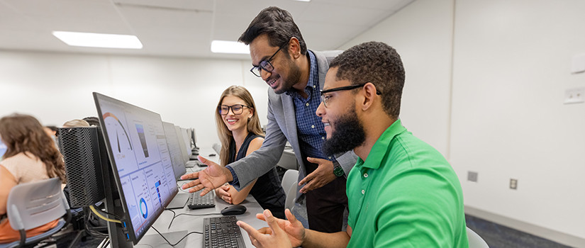 A faculty member gives instruction to two students in a computer lab