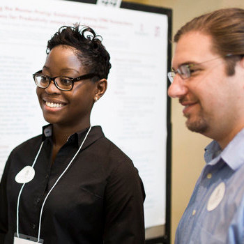 A student and faculty member stand in front of a projector screen.