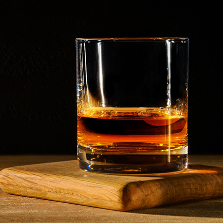 Glass with whisky on wooden table and black background.