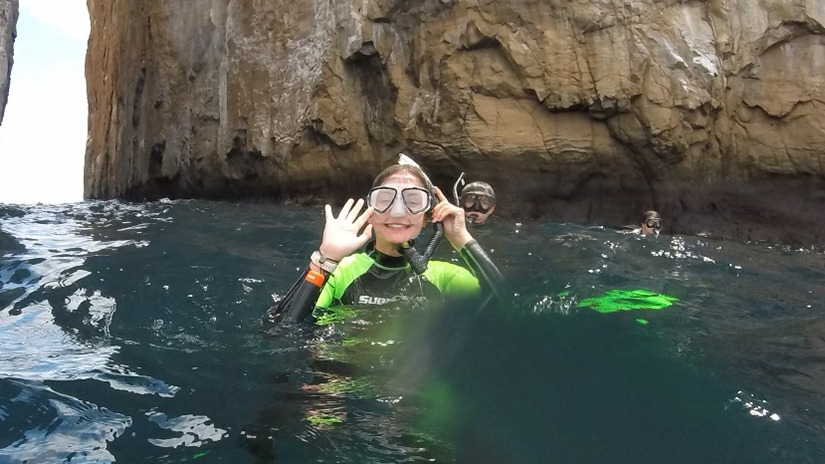 A student in snorkeling gear waves to the camera while enjoying the water in the Galápagos Islands.