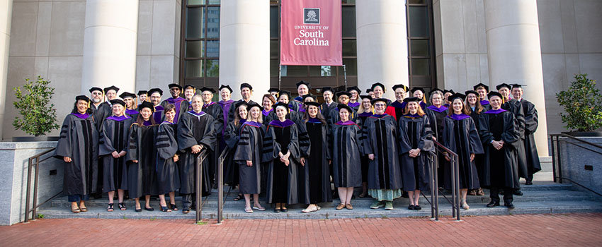 Group shot of faculty taken in their academic regalia on the front steps of the School of Law.