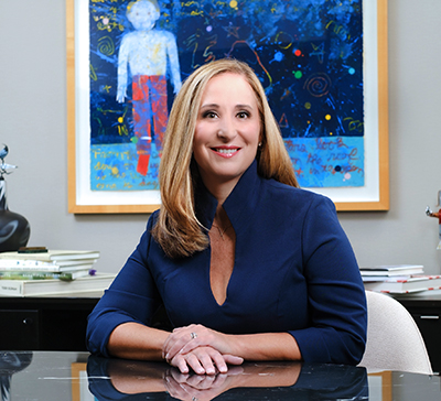 Alex Chastain sitting at a table wearing blue shirt; artwork hanging behind her