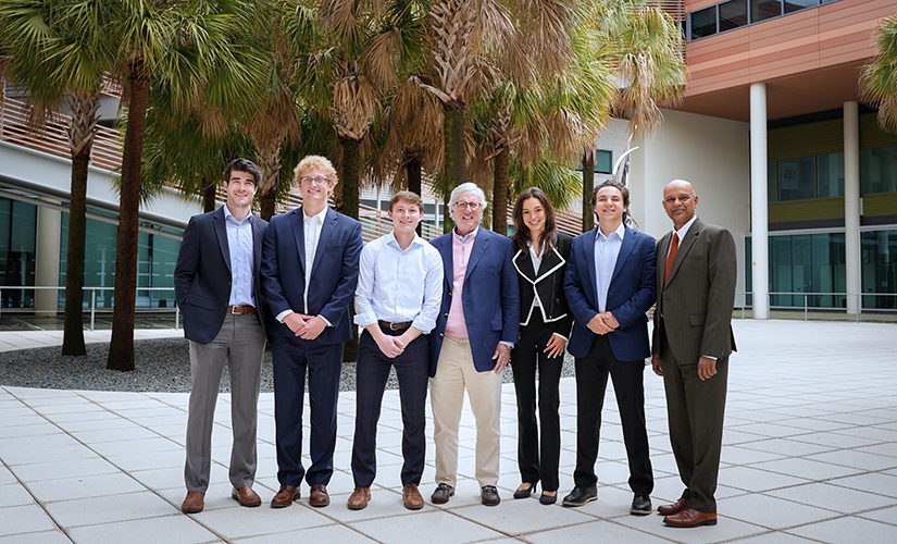 John Harloe with Dean Rohit Verma and the 2023-24 recipients of the S. Travis Pritchett Investments Scholarship; group is standing in the Moore School Courtyard with palmetto trees in the background