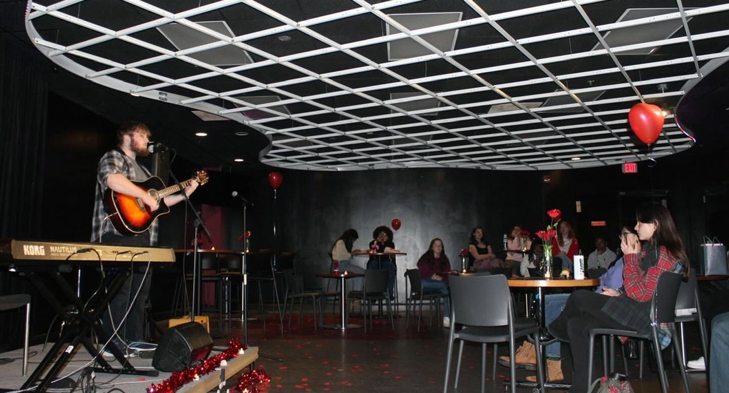 A band plays on stage while students sit at tables listening to the music.