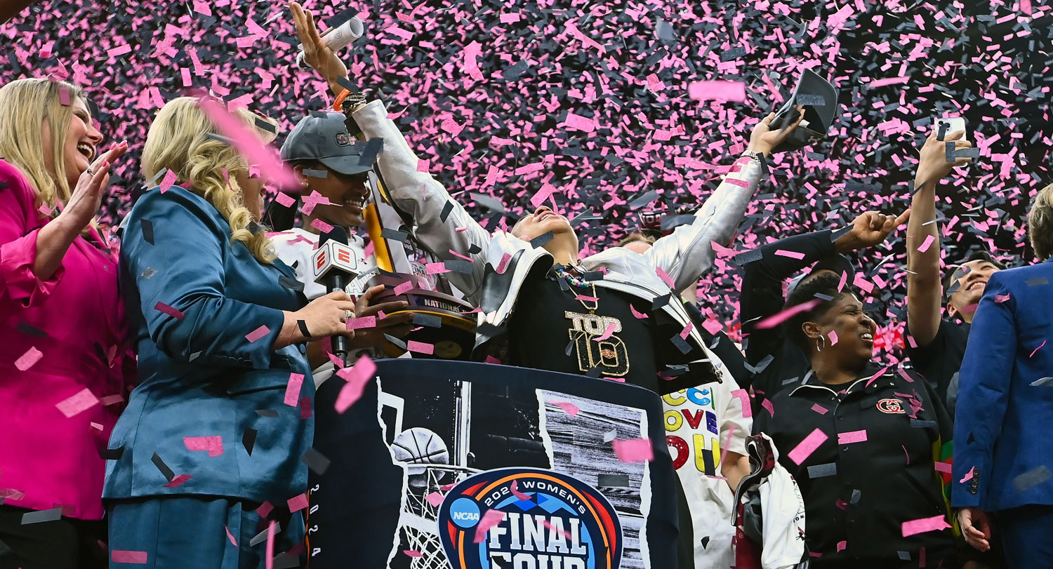 woman stands in a shower of confetti with hands raised to the ceiling