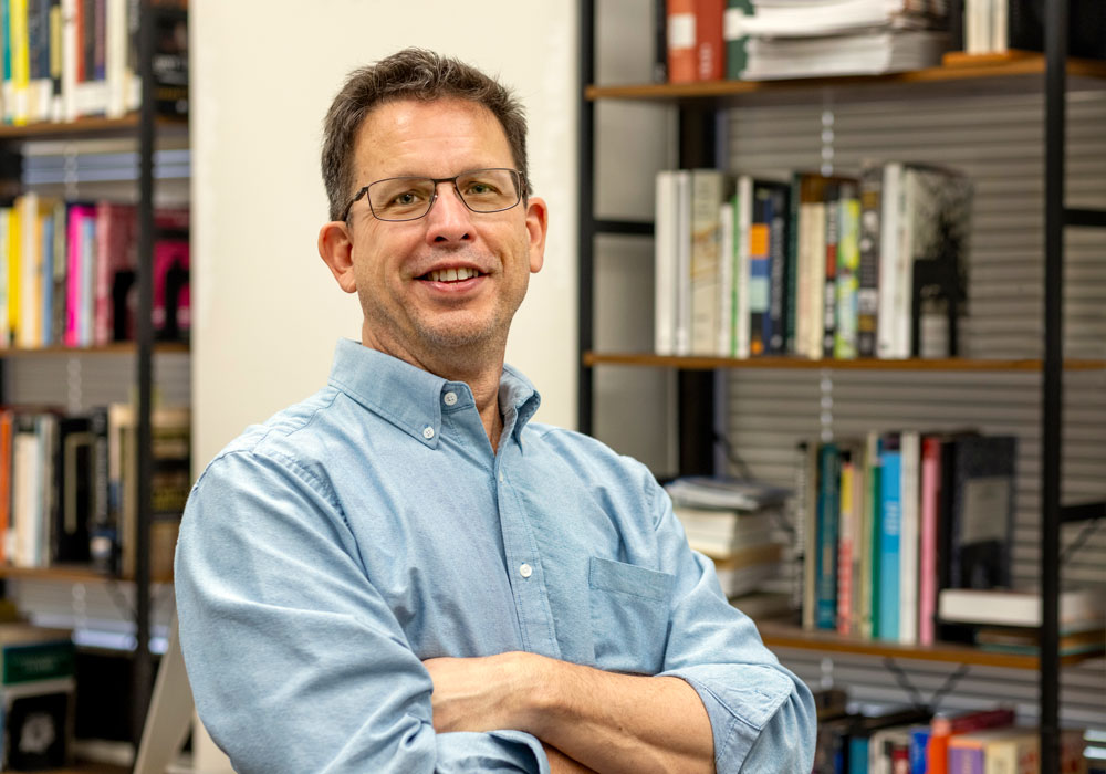 man stands in front of a bookcase full of books