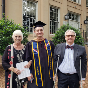 William Brown wearing a graduation cap and gown stands with his parents