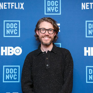 man stands in front of a backdrop with logos for DOC/NYC, HBO and Netflix