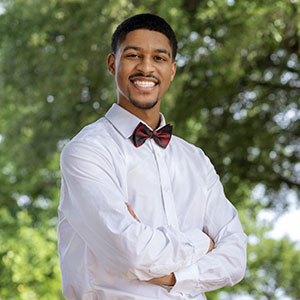 A man smiling with his arms crossed over his torso in an outdoor area.