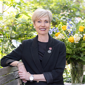 Susan Elkins sits on a bench on USC's historic Horseshoe with a vase of yellow, lavendar and white flowers over her left shoulder