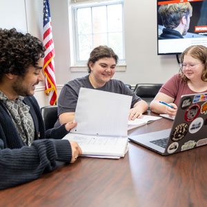 Three CIC students study in front of a laptop in a classroom.