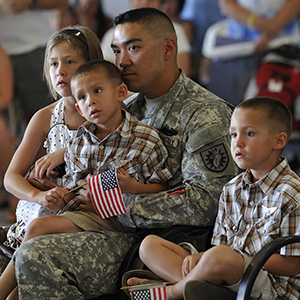 A man wearing a military uniform sits and holds a small boy on his lap, while a girl and boy sit close to him. 